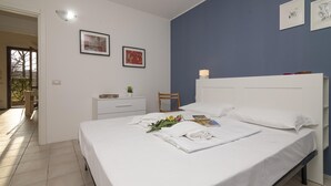 A neatly made bed with white linens, a bedside table with a lamp, and a framed picture on the wall. - Mobilehome in Porlezza am Luganersee (Porlezza)