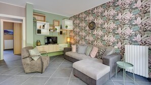 A modern living room with a sofa, armchair, and a small table. There is a TV and a cabinet with shelves. - Mobilehome in Porlezza am Luganersee (Porlezza)