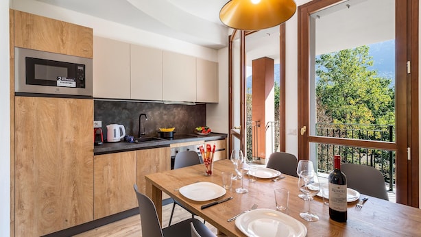 A modern kitchen with wooden cabinets, a built-in microwave, and a dining area with a table set for two. - Mobilehome in Porlezza am Luganersee (Porlezza)