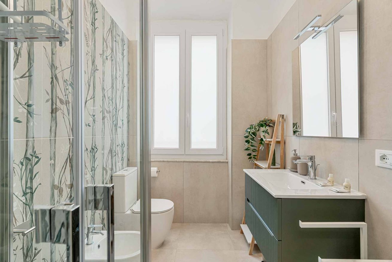 Ein modernes Badezimmer mit Duschkabine aus Glas, Toilette, Waschbecken mit Spiegel und einem Fenster für natürliches Licht.