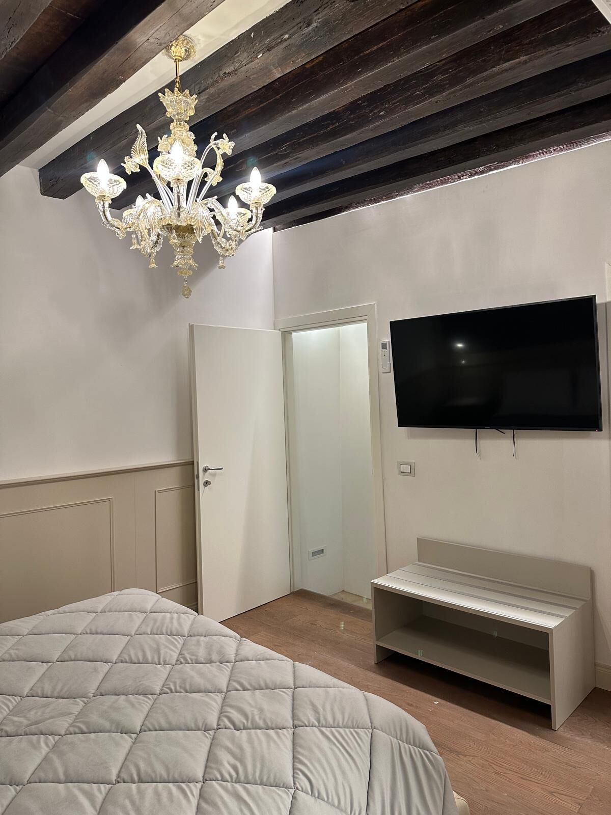 Ein Schlafzimmer mit einem Bett, einem an der Wand befestigten Fernseher, einer Sitzbank und einer Chandelier.