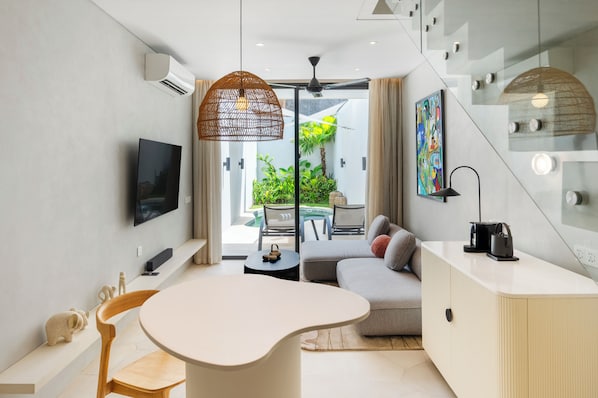 Una sala de estar moderna con un sofá, una mesa de centro, un televisor y una zona de comedor con sillas.