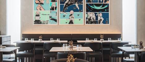 Un restaurant au décor moderne, avec une longue table à manger entourée de chaises, un vase décoratif placé au centre et des œuvres d’art encadrées accrochées au mur.