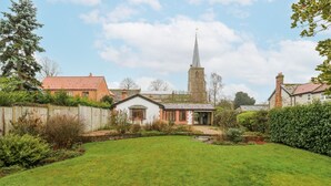 Een woonwijk met een gazon, een klein wit huis met een rood dak en een kerktoren in de verte.