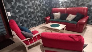 Una habitación con una pared de estampado geométrico, un sofá de cuero rojo, un sillón blanco y una pequeña mesa blanca.