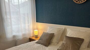 Un letto con una coperta a motivi, due decorazioni tessute appese al muro, una lampada da comodino e una finestra con tende leggere.