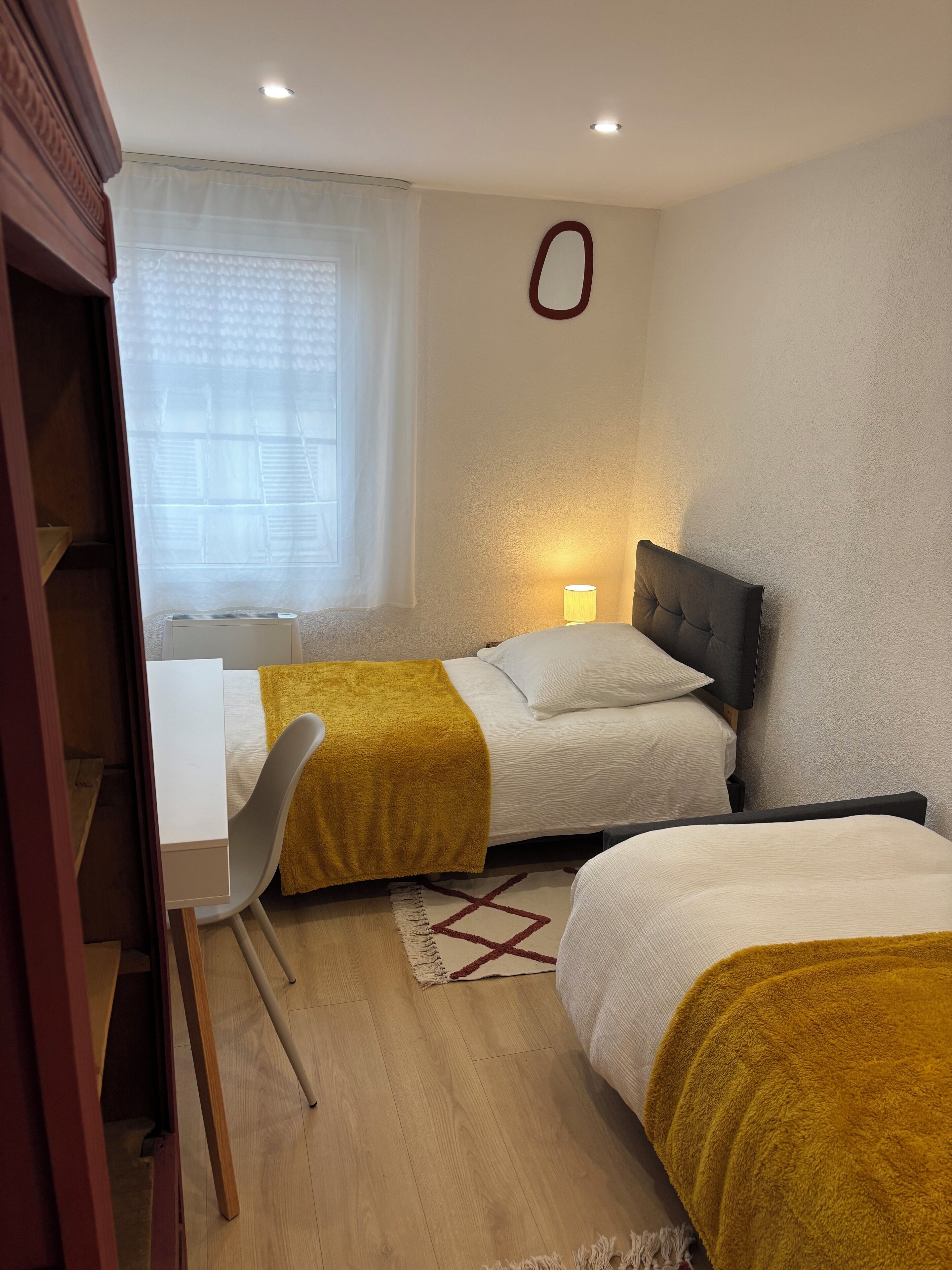Une chambre avec deux lits, un bureau, une chaise, une lampe et une fenêtre avec des rideaux.