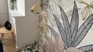 A room with a patterned wallpaper, a floor lamp, a round table with a vase, and a chair. - Super-central apartment for family or business (Châlons-en-Champagne)
