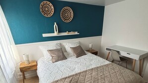 A bedroom with a bed, bedside tables, a desk, and a blue accent wall. - Super-central apartment for family or business (Châlons-en-Champagne)