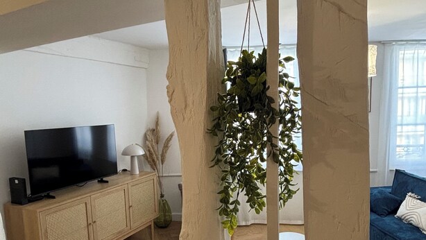 A living room with a television, wooden cabinet, hanging plant, and a blue sofa. - Super-central apartment for family or business (Châlons-en-Champagne)