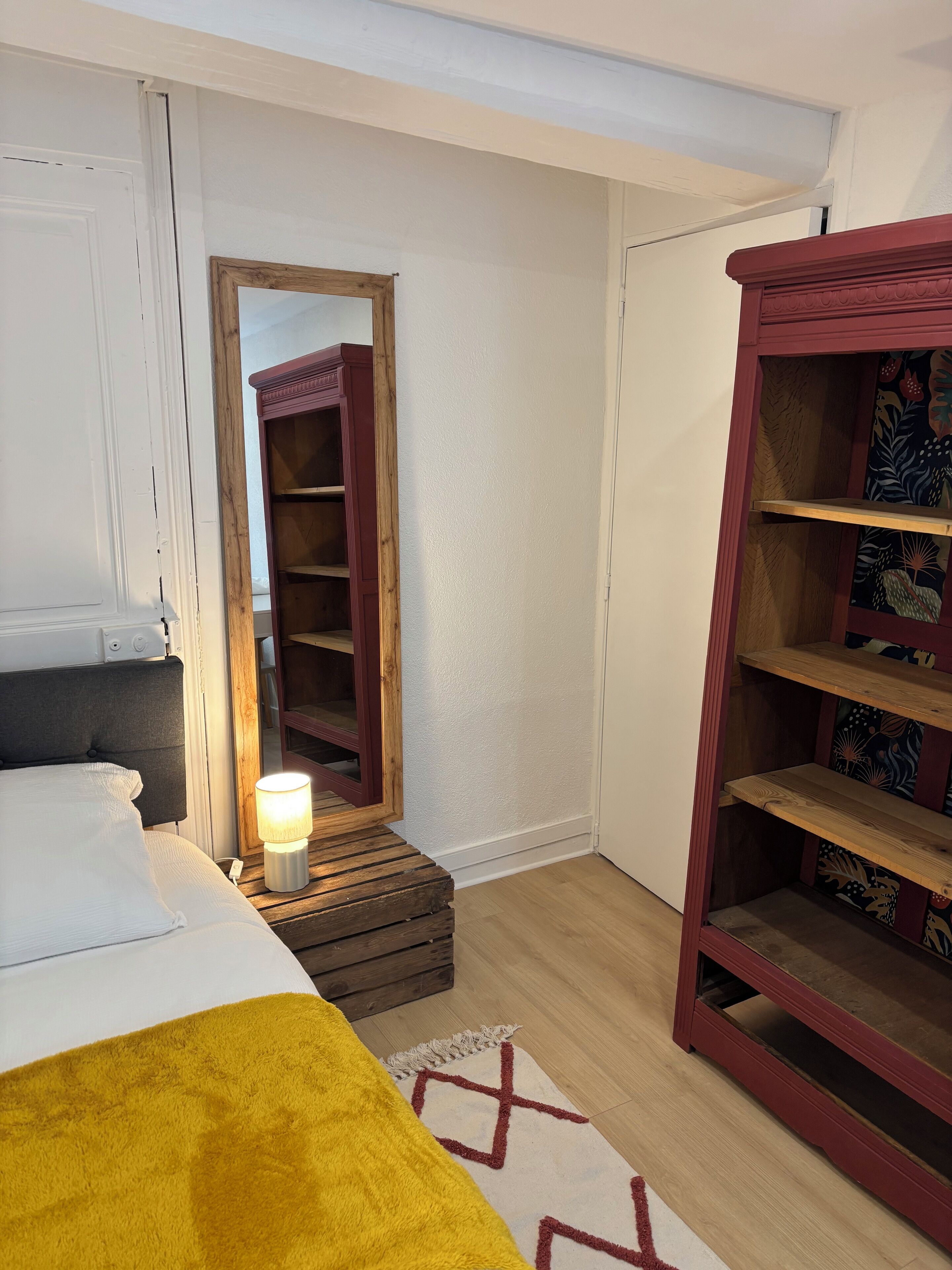 A bedroom with a bed, bedside lamp, wooden nightstand, and a wardrobe.