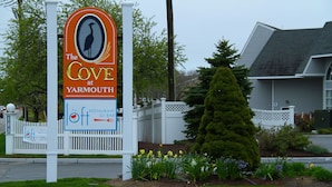 Une enseigne pour le restaurant-bar The Cove, situé à Yarmouth, avec une clôture en bois peinte en blanc et un jardin bien entretenu agrémenté de fleurs jaunes.