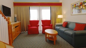 Une chambre d’hôtel avec un canapé, deux fauteuils, une petite table, un téléviseur, une lampe et un tableau au mur.