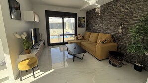 A modern living room with a sofa, coffee table, and a TV. There is a sliding glass door leading to a balcony with a pool. - Casa Montgavina, villa in the heart of Vistabella Golf (Entrenaranjos)