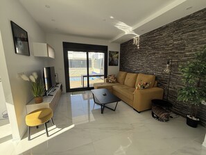 Een moderne woonkamer met een bank, salontafel en een televisie. Er is een schuifdeur die leidt naar een balkon met een zwembad.