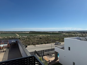 A rooftop terrace with outdoor furniture, a swimming pool, and a view of agricultural fields and distant mountains.