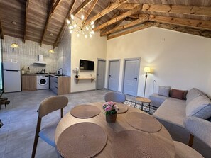 A modern kitchen with a built-in washing machine, a dining area with a round table and chairs, and a living area with a sofa and a lamp. - Hg Barn House Gabala (Gabala)
