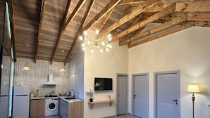 A spacious living area with a high ceiling, exposed wooden beams, a kitchen with modern appliances, a dining table with woven placemats, and a floor lamp. - Hg Barn House Gabala (Gabala)