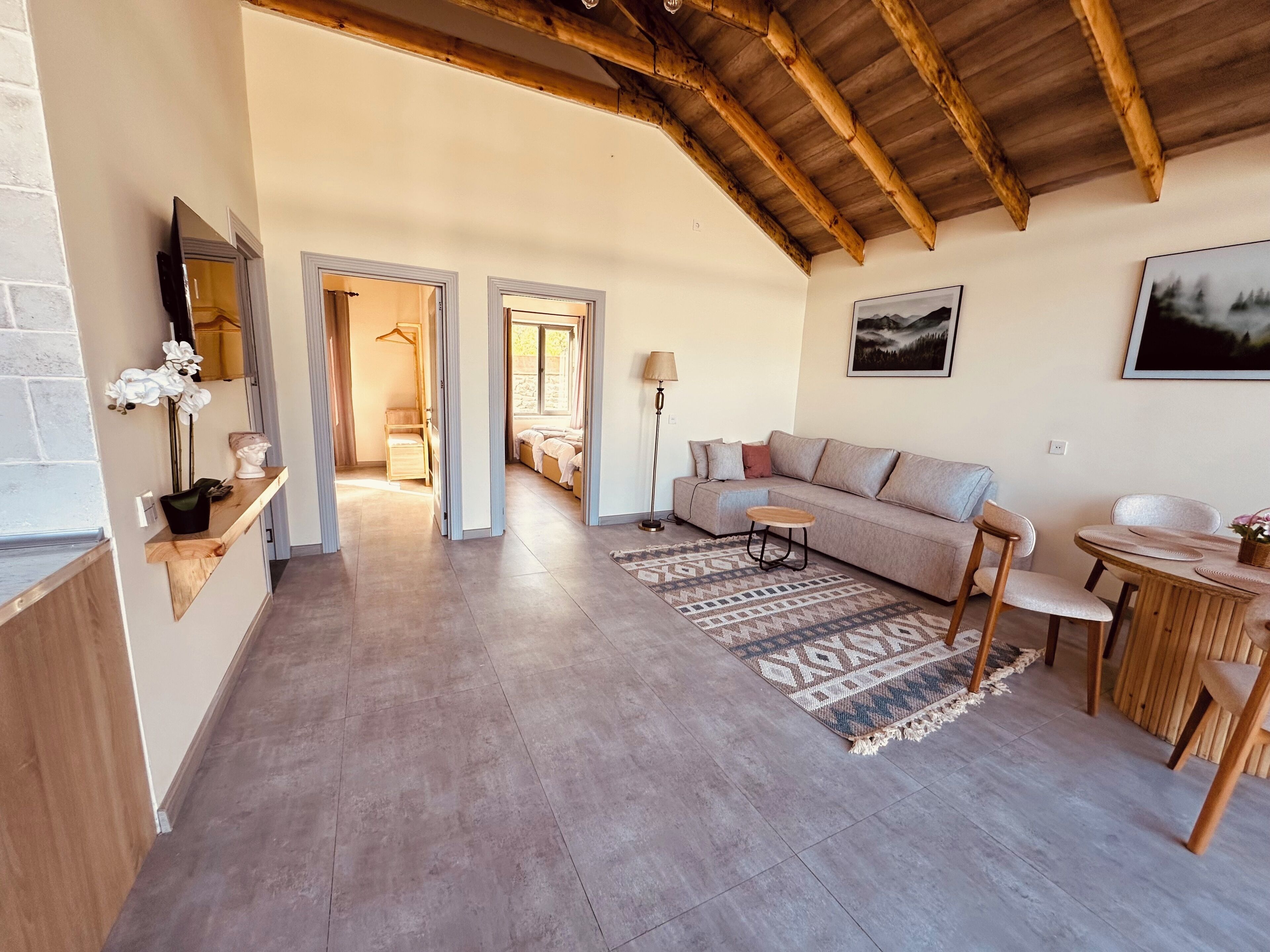 A spacious living area with a wooden ceiling, a sofa, a coffee table, and a dining table with chairs.
