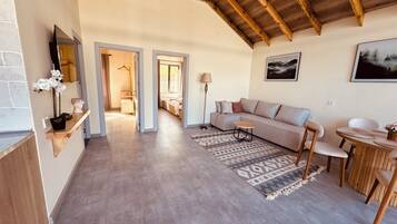 A spacious living area with a wooden ceiling, a sofa, a coffee table, and a dining table with chairs.