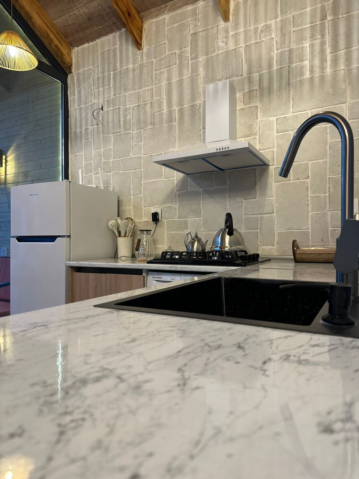 A kitchen with a marble countertop, a gas stove, a sink, a refrigerator, and a wooden ceiling.