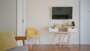 Una sala moderna con un sofá, un sillón amarillo, una mesita de madera, un televisor montado en la pared y una puerta blanca.