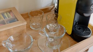 Una mesa de madera con una cafetera amarilla, dos tazas de vidrio transparente y un marco con una fotografía.