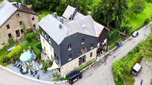 A two-story building with a dark roof and light walls, located at a street corner with a small outdoor seating area. - Dog-friendly House With Sauna, Bubble Bath (Bouillon)