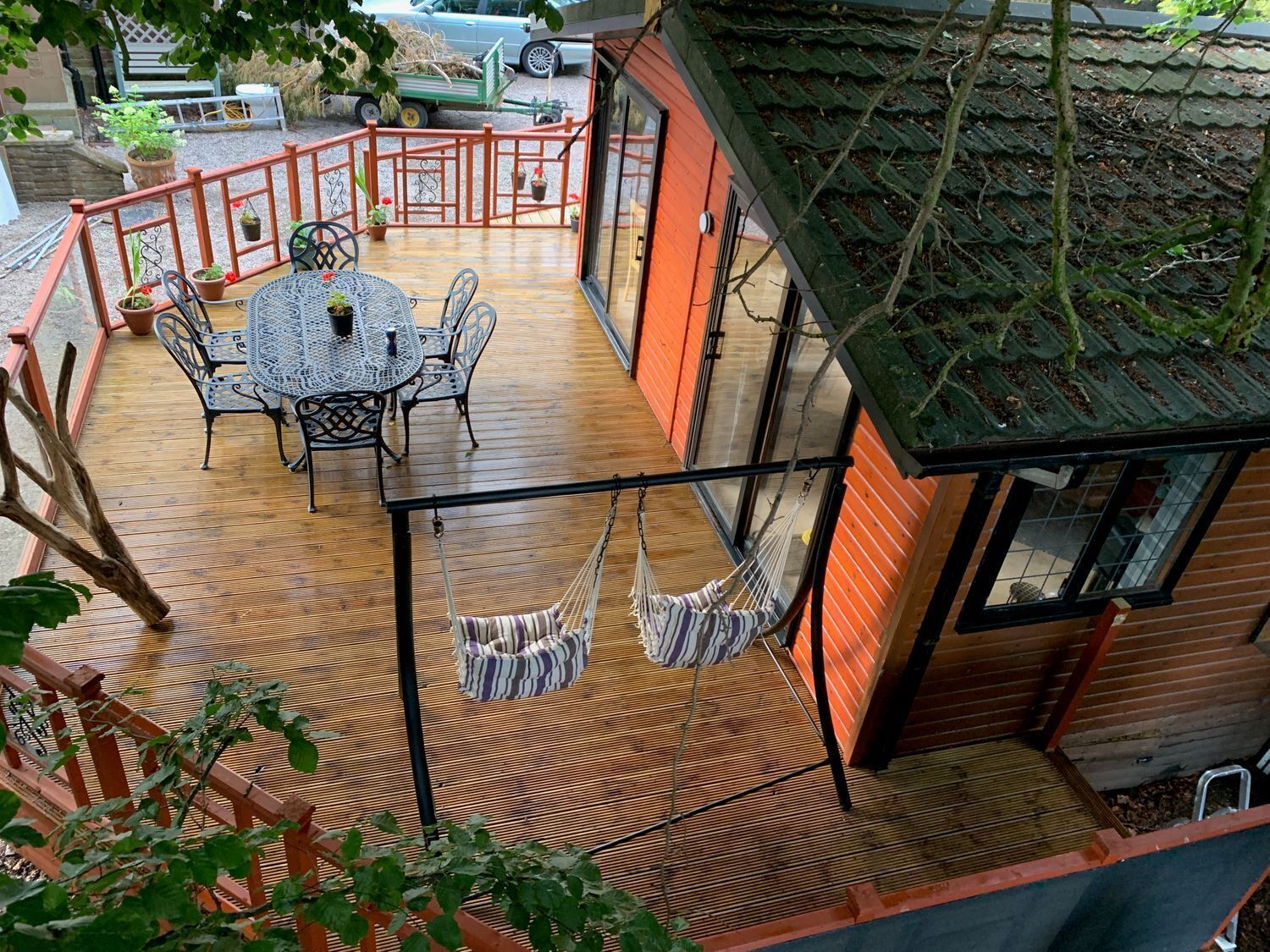 A wooden deck with a table and chairs, a hammock, and a small wooden structure with a window.