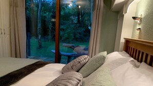 Une chambre avec une grande fenêtre, un lit recouvert de draps blancs et une vue sur une zone boisée.