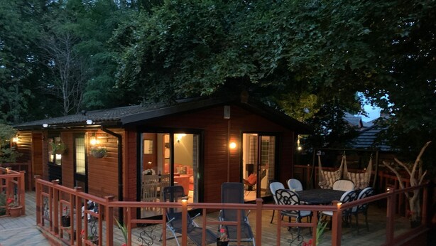 Une cabane en bois dotée d’une terrasse, aménagée avec des meubles de jardin et une table.