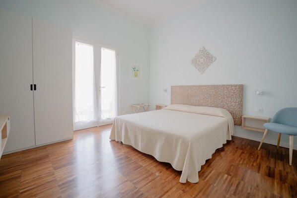 Une chambre avec un grand lit, une armoire, une chaise et une porte donnant sur un balcon.
