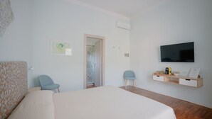 Un dormitorio con una cama, dos sillas, un televisor y una estantería con objetos.