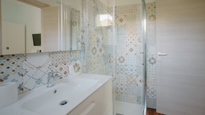 Un baño con cabina de ducha de vidrio, un lavamanos blanco y baldosas con diseño.