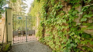 Una entrada protegida por un portón metálico, un camino de grava y un muro cubierto de hiedra verde.