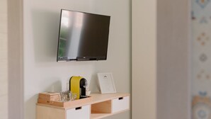 Un televisor montado en la pared sobre una repisa de madera con una cafetera, vasos y un menú enmarcado.
