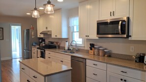 Una cocina moderna con armarios blancos, electrodomésticos de acero inoxidable e iluminación colgante.