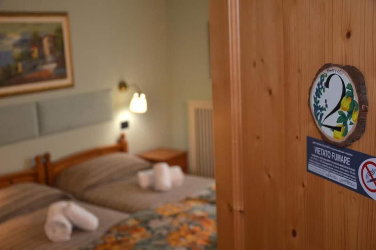 A hotel room with a bed, a nightstand, and a wall-mounted lamp. There is a sign on the door indicating room number 2 and a no-smoking sign.