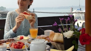 A person dining at an outdoor table with a view of the water and boats, featuring breakfast items like toast, fruit, and a teapot. - Porticciolo del Campanello (Castelnuovo del Garda)