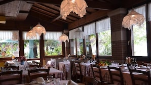 A restaurant with multiple tables set for dining, featuring lace-covered hanging lamps and large windows with curtains. - Porticciolo del Campanello (Castelnuovo del Garda)