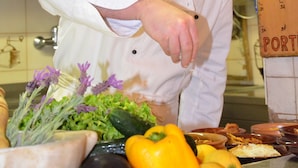 A chef in a white uniform and blue hat, working with vegetables on a kitchen counter. - Porticciolo del Campanello (Castelnuovo del Garda)