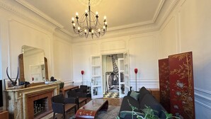 A spacious living room with a fireplace, a chandelier, striped chairs, a sofa, and a large mirror. - Haut de la Canebière Magnifique Appartement 4* (Marseille)