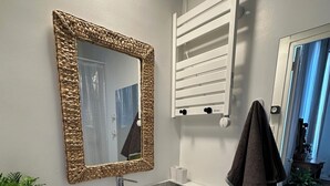 A modern bathroom with a white vanity, a large mirror with a woven frame, a towel rack, and a potted plant. - Haut de la Canebière Magnifique Appartement 4* (Marseille)