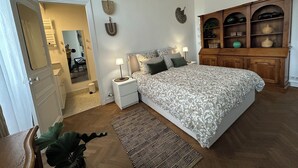 A bedroom with a large bed, a wooden cabinet with shelves, a small bedside table with a lamp, and a mirror on the wall. - Haut de la Canebière Magnifique Appartement 4* (Marseille)