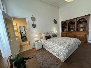 Ein Schlafzimmer mit einem großen Bett, einem Holzkasten mit Regalen, einem kleinen Nachttisch mit Lampe und einem Spiegel an der Wand.