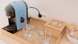 Una cafetera, dos vasos con pajitas, una bandeja de madera, un cuadro enmarco y un bol de pasteles sobre una mesa de madera.