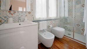 Un baño moderno con tocador blanco, bidé, inodoro y cabina de ducha de vidrio.