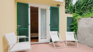 Un patio con dos sillones blancos y una puerta con contraventanas verdes.