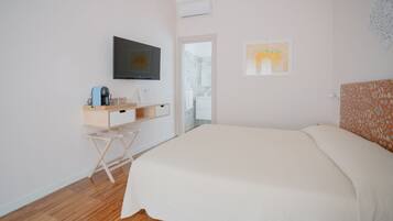 Ein Schlafzimmer mit Bett, einem an der Wand montierten Fernseher, einem kleinen Schreibtisch mit Stuhl und einer Tür, die auf einen Balkon führt.