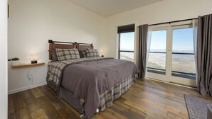 Een slaapkamer met een groot bed, een nachtkastje, een lamp en uitzicht op het landschap door het raam.